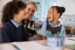 teacher smiling at two children at a table.