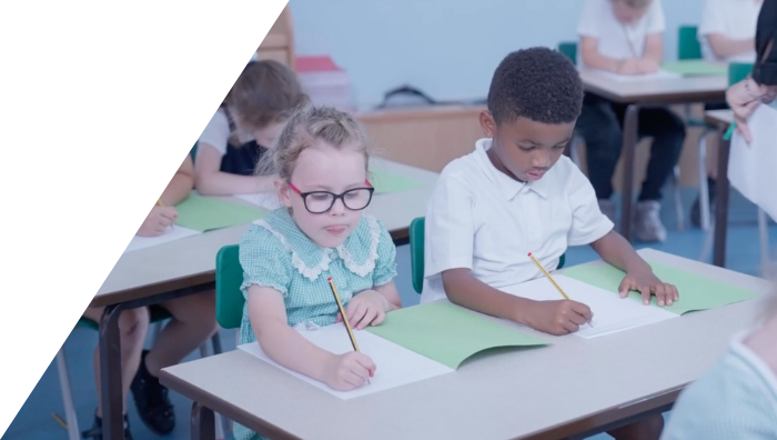 two students sitting at a table writing in workbooks